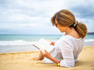 Woman sitting on beach reading book
