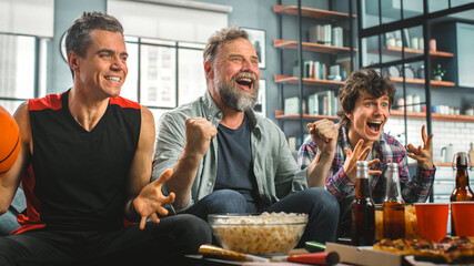 At Home Three Happy Basketball Fans Sitting on a Couch Watch Game on TV, Celebrate Scoring, their...