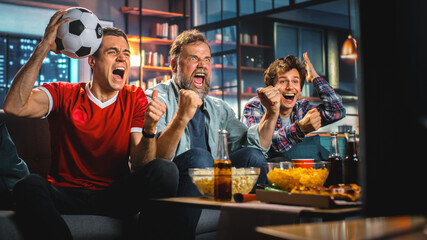 Night At Home: Three Joyful Soccer Fans on a Couch Watch Game on TV, Celebrate Victory when Sports Team Wins Championship. Friends Cheer for Favourite Football Club Play. © Gorodenkoff