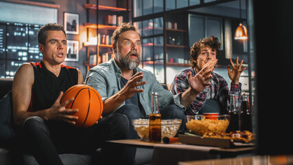 At Home Three Joyful Basketball Fans Sitting on a Couch Watch Game on TV, Celebrate Victory when...