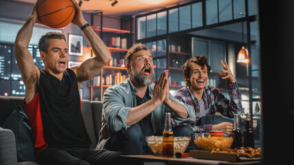 At Home Three Joyful Basketball Fans Sitting on a Couch Watch Game on TV, Celebrate Victory when...