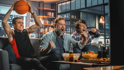 At Home Three Joyful Basketball Fans Sitting on a Couch Watch Game on TV, Celebrate Victory when...
