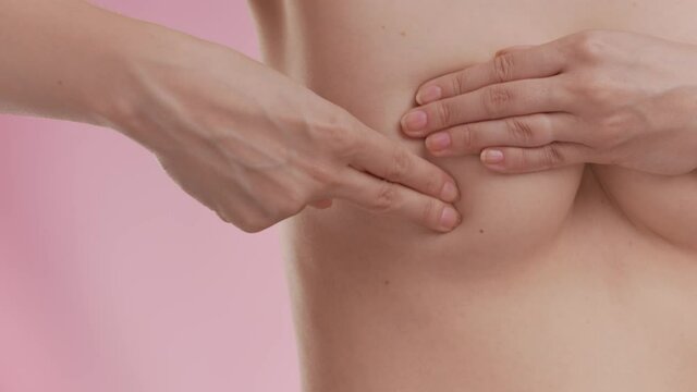 Breast cancer awareness. Young topless woman doing breast self-exam (BSE) on pink background. Checking up breast changes, possible lumps, distortions or swelling. Healthcare and medical concept.