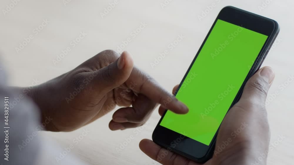 Poster close up shot of black guy scrolling touchscreen of modern smartphone, gadget with green chroma key 