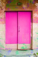 The old wooden doors are bright pink and the wall is covered with paint.