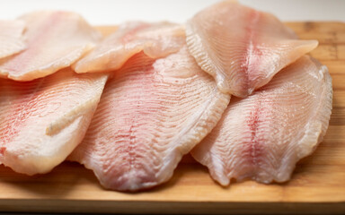 pieces of raw fish, tilapia on a wooden surface. Fresh fish, seafood, vitamins, d3. The benefits or harms of seafood, deficiency