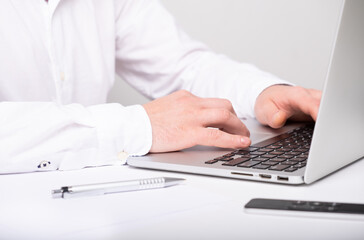 close up of male hands typing on laptop keyboard while working at white desk