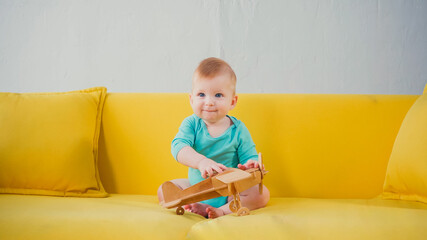 happy infant boy sitting on sofa and playing with wooden biplane