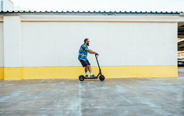 Obraz premium Young hipster man driving electric scooter in bright sunny day. Ecological transportation concept.