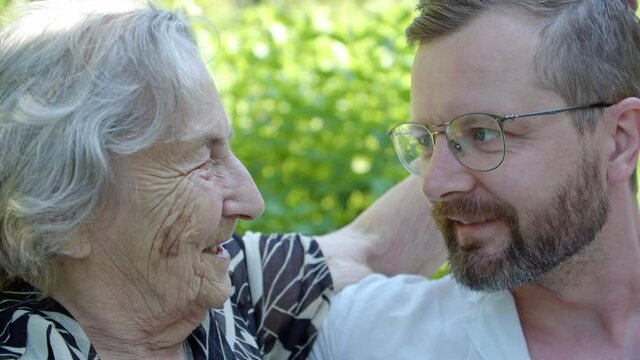 an old woman in the garden looks at her adult grandson and strokes on the head, the joy of meeting laughter and smiles, the same eye color
