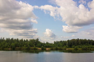 Summer landscape with a beautiful lake with fir trees and forested mountains against a cloudy sky