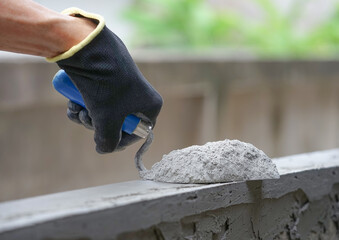 hand of industrial bricklayer hold aluminium trowel scoop mortar powder put on a brick block wall...