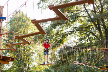 Boy In Adventure Park having fun in high wire park. Child climbs in a rope park. Preteen Boy On A Ropes Course. Male toddler on zip line. Boy having a fun on Climbing Frame. Boyscout on a tree. Summer