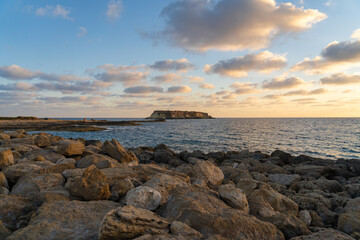 Rocky shore of Agios Georgios Cyprus. View of the island Yeronisos. Sunset at Agios Georgios Pegeias harbor in Paphos, Cyprus. The Akamas peninsula and the island of Geronisos