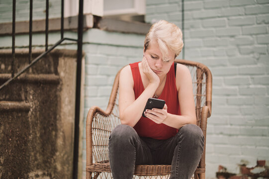 Young person intently looking at cell phone sitting in chair - Powered by Adobe