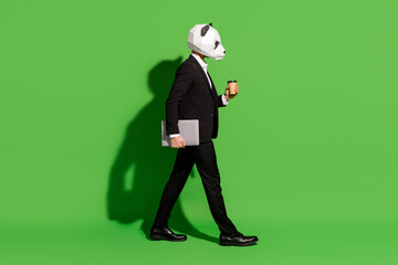 Photo of worker guy walk hold takeaway coffee cup laptop wear panda head black suit isolated on...