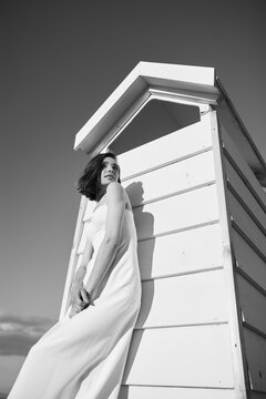 black and white photo girl in a white dress in full length stands around a wooden house