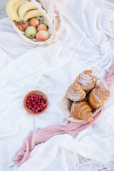 Fototapeta na wymiar Red berries on plate near croissants and flowers on white blanket, picnic
