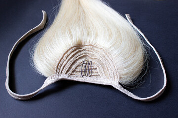 Blonde natural hair for extensions up close-up on a black background. A ponytail made of hair with dark corners and light ties.