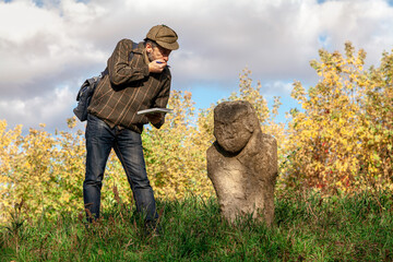 Tourist stands next to stone sculpture on mound