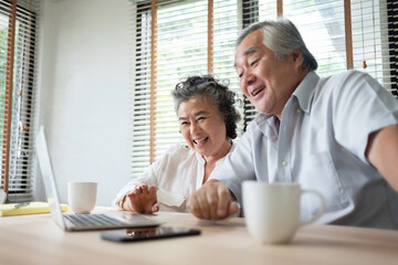 Cheerful Asian Senior couple having video chat with their family on Laptop computer on table at home