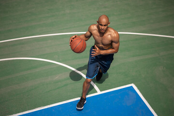 Fototapeta premium Strong muscular african-american male basketball player training at street public stadium, sport court or palyground outdoors. Concept of healthy active lifestyle, motion, hobby.