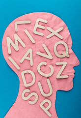 Head silhouette made of paper and white wooden letters. Crumpled pink paper shaped as a human head with copy space on blue paper background.
