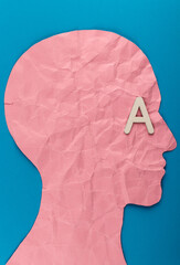 Head silhouette made of paper and white wooden letter. Crumpled pink paper shaped as a human head...