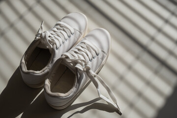 Close-up of women's white leather sneakers in the shade of the blinds.