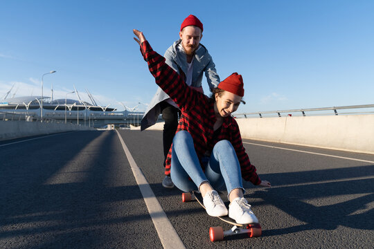 Stylish man and woman longboarding enjoy time together. Young couple in romantic relationship skating on longboard happy laughing dressed in street style clothes. Urban fashion and trendy activity