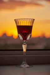 A glass of red wine on the windowsill against the background of the sunset.