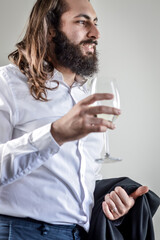 Portrait of a young middle eastern businessman with beard and long hair holding a glass of white wine and his jacket on his arm