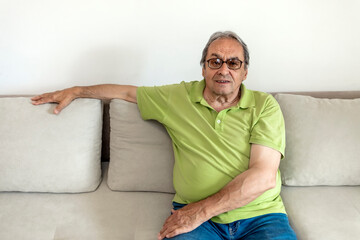 Photo of a handsome senior man relaxing on a sofa at home alone. Smiling senior man resting at home. Relaxed happy grey haired mature old man enjoying free lazy weekend time on sofa. Copy space.