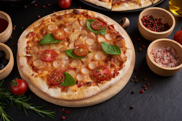 Italian pizza and pizza cooking ingredients on black concrete background. Tomatoes on vine, mozzarella, black olives, herbs and spices. Mixture pizza Italian food. Copy Space. Top view.