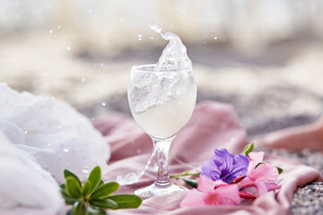 Explosion of tonic cocktail in wine glass on beach with flowers. Summer cocktail. Delicate silk materials and bokeh background. Refreshing summer concept