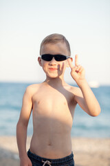 Fototapeta premium Portrait with little boy in sunglasses standing on the beach with blurry background by the sea