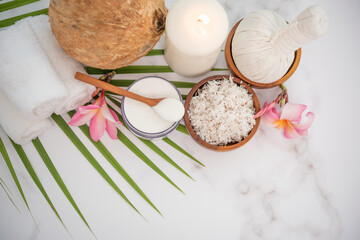 Coconut oil, tropical leaves and fresh coconuts. Spa coconut products on light wooden background. Spa still life of organic cosmetics with coconuts on a light wooden background, body care concept.