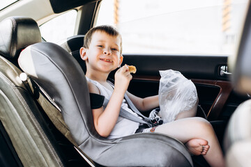 Child sitting in a car seat and eating bread. Funny little boy with a blurred face looking at the...