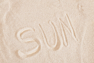 Fototapeta na wymiar word sun on sandy background, texture of light sand top view