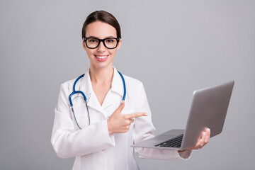 Photo portrait young nurse with sthethoscope smiling showing finger laptop isolated grey color...