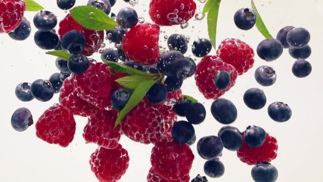 Raspberry, blueberry, mint leaves splash floating in the water, white background