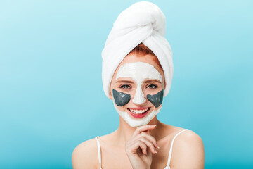 Front view of blissful caucasian woman with face mask. Studio shot of pleasant girl with towel on head posing on blue background.