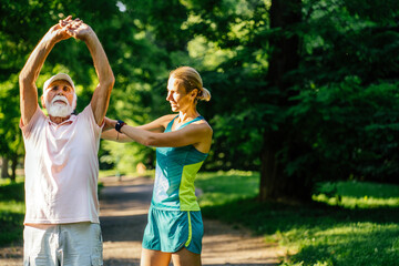 Old man training with physiotherapist using at park. Female therapist assisting senior man with exercises in nursing home, outdoor. Elderly patient raised stretched hands.