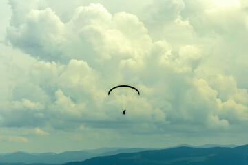 Silhouette of a paraglider flying in the cloudy sky. Extreme sport. Extreme vacation.