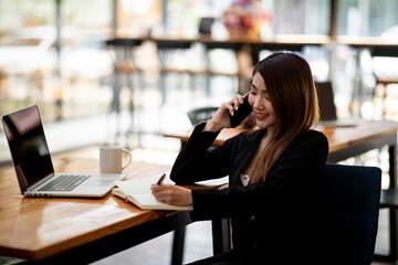 Portrait of businesswoman wearing black jacket, she is working on the computer at coffee shop.
