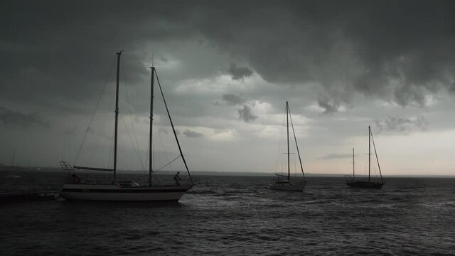 Three yachts sway in the sea on the waves near the pier against the backdrop of cloudy sky and lightning