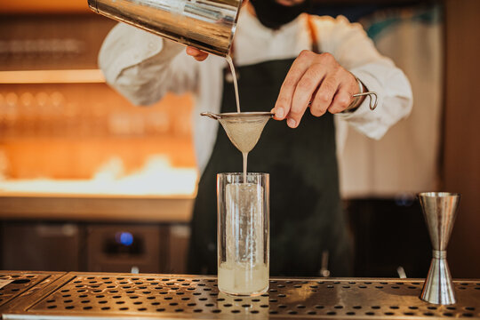 Close up shot of a bartender in a green apron making a cocktail. Concept of hospitality, leisure, restaurant and mixology. Focus on hands and a glass