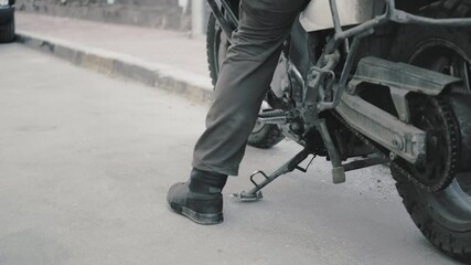 Biker puts the footboard at the enduro motorcycle and gets off the vehicle. The city, urban landscape, asphalt and stones. Concept of travel, leisure sports and hobbies