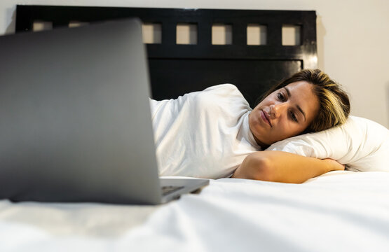 Young Hispanic Woman Lying In Bed Watching Her Favorite Series On Her Laptop