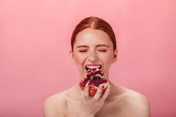 Fotobehang Front view of nude girl eating garnet. Studio shot of woman with pomegranate isolated on pink background. © Look!